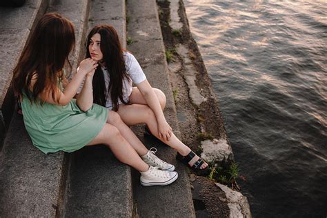 Cute Lesbian Couple Talking While Sitting On Steps By River In City