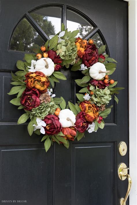A Wreath On The Front Door With Flowers And Greenery Hanging From Its Side