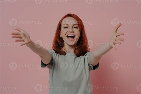 friendly happy ginger woman stretching arms for hug and smiling cheerfully isolated on pink
