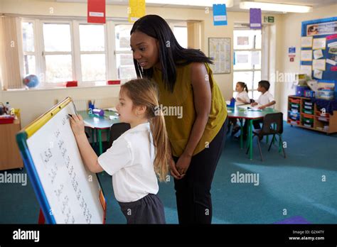 Elementary School Pupil Writing On Whiteboard In Classroom Stock Photo