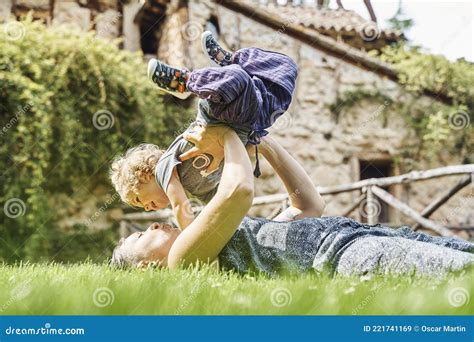 Young Mother Lying On The Grass Lifting Her Daughter Overhead Stock