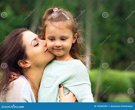 Beautiful Mother Hugging And Kissing Her Cute Small Daughter On Summer Green Grass Background