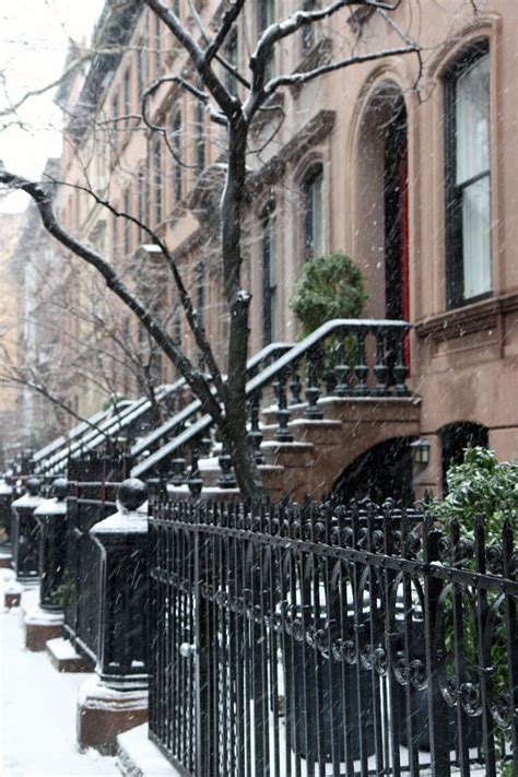 A Row Of Browns Houses On A Snowy Day With Snow Falling From The Roof