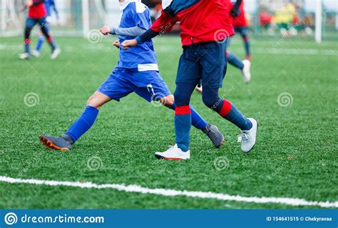 Boys In Red And Blue Sportswear Plays Football On Field Dribbles Ball