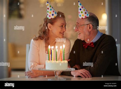 Portrait Of Loving Senior Couple Celebrating Birthday Together Sitting At Table With Cake And