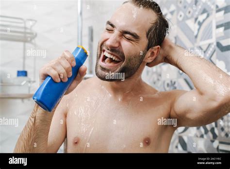 Attractive Young Cheerful Man Singing While Washing In The Shower Holding Shampoo Bottle Stock