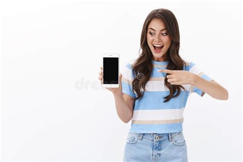 Amused Cheerful Young Woman Introduce Smartphone App Hold Mobile Phone Pointing And Looking