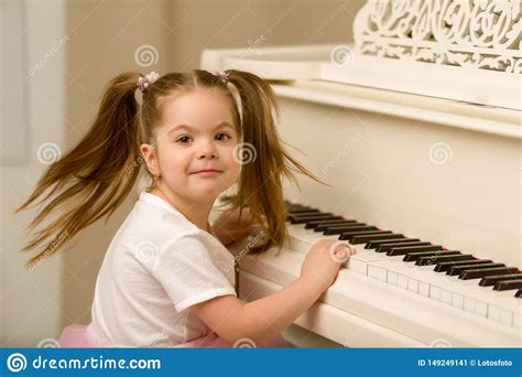 Beautiful Little Girl Is Playing On A White Grand Piano Stock Image
