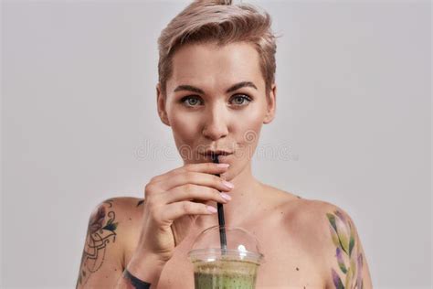 Attractive Tattooed Woman With Pierced Nose And Short Hair Looking At Camera While Drinking