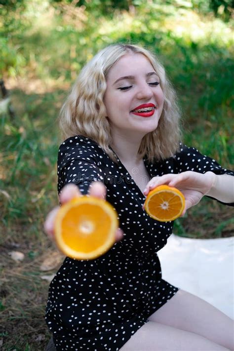 Portrait Of A Charming Blonde Teenage Girl With A Fresh Orange Outdoors