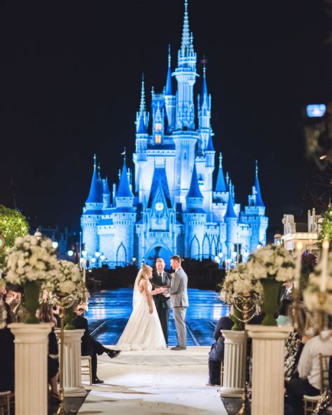 A Bride And Groom Standing In Front Of A Castle At Night With The Lights On