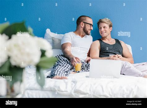 Gay Couple Lying In Bed Using Laptop Stock Photo Alamy