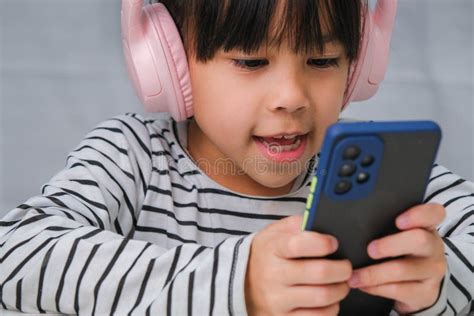 Cute Elementary School Girl Wearing Headphones Holding A Smartphone