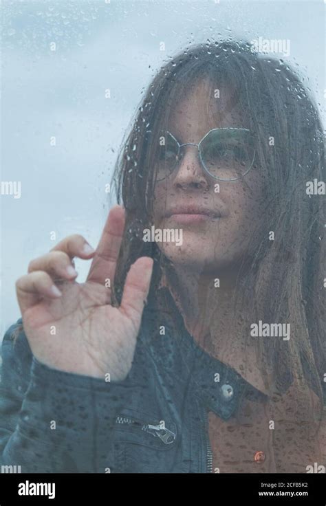 Portrait Of Beautiful Woman With Glasses Looking Out Of Wet Window On