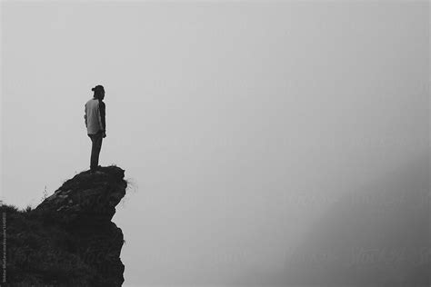 Black And White Image Of A Man Standing At The Edge Of The Cliff By