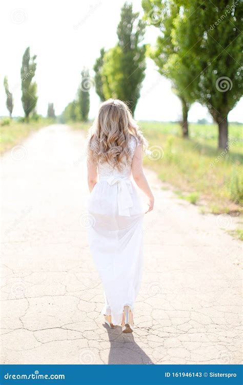 Back View Of Young Woman Wearing White Dress Walking On Road Stock