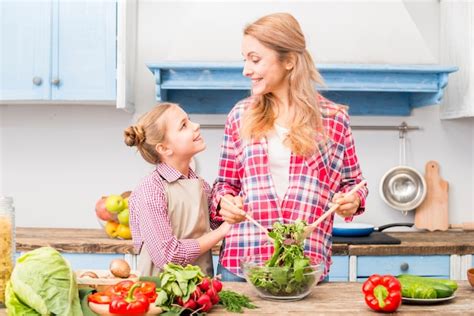 Hija Mirando A Su Madre Preparando La Ensalada En La Cocina Foto Gratis