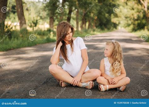 Attractive Mom And Blonde Hair Daughter Sits On Road Near Big Alley