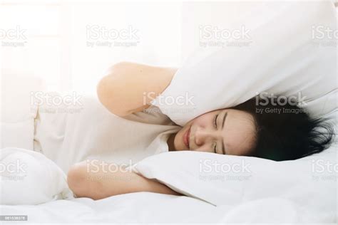 Young Asian Woman Lying In Bed And Covering Her Ears With Pillows From