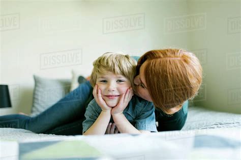 Mother Kissing Her Sons Cheek On Bed Stock Photo Dissolve