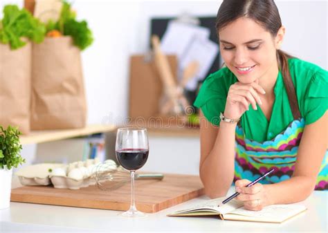 Happy Beautiful Woman Standing In Her Kitchen Writing On A Notebook At