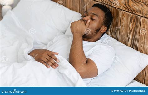 Sleepy Black Man Yawning Awakening Lying In Bed At Home Stock Photo