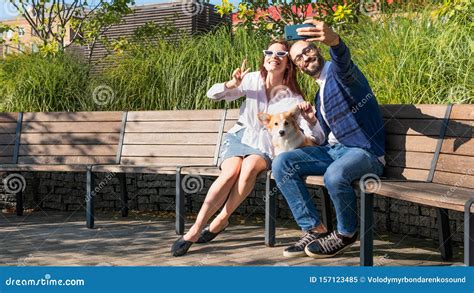 The Happy Couple Are Sitting On The Bench In The Park With Little Dog