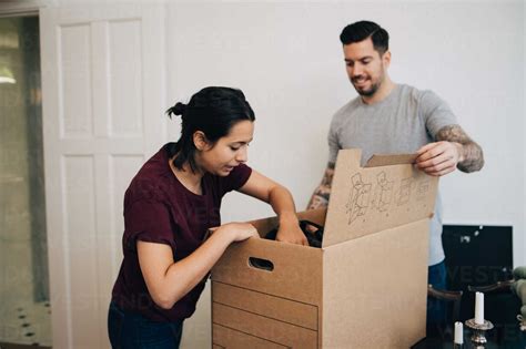Man Assisting Woman In Unpacking Box At New House Stock Photo
