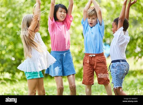 Group Of Kids As Friends Play Together In The Park And Raise Hands