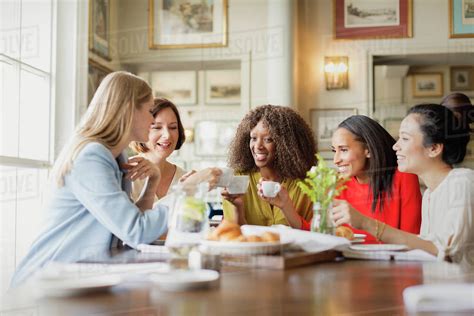 Smiling Women Drinking Coffee And Talking At Restaurant Table Stock Photo Dissolve