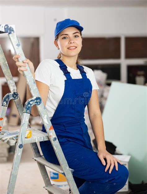 Positive Builder Woman In Blue Overalls Next To Stepladder Stock Image
