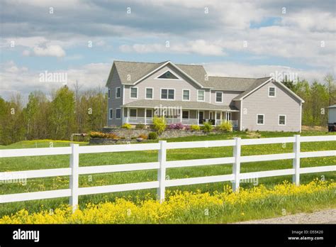 Two Story Farmhouse Style Home And White Fence In Rural Maine Stock