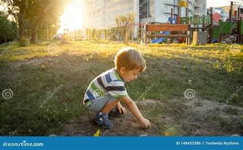 Photo Of Cute Little Toddler Boy Sitting In Park And Digging Sand Stock