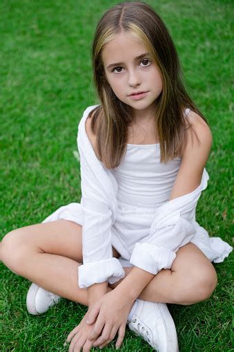 Pretty Tween Girl In White Clothes Sitting On Green Grass Outside In