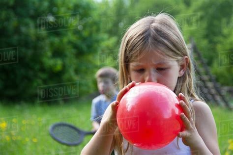 Close Portrait Of Young Girl Blowing Up Red Balloon Stock Photo