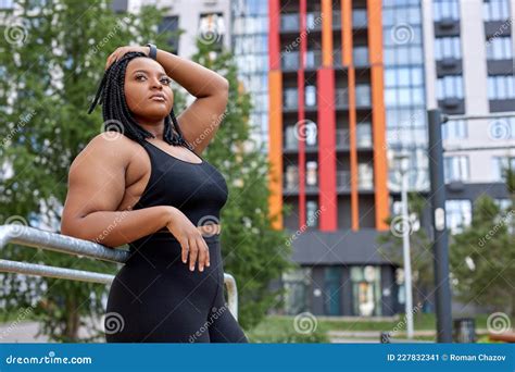 side view portrait of confident fat plus size female in sportive outfit posing outdoors stock