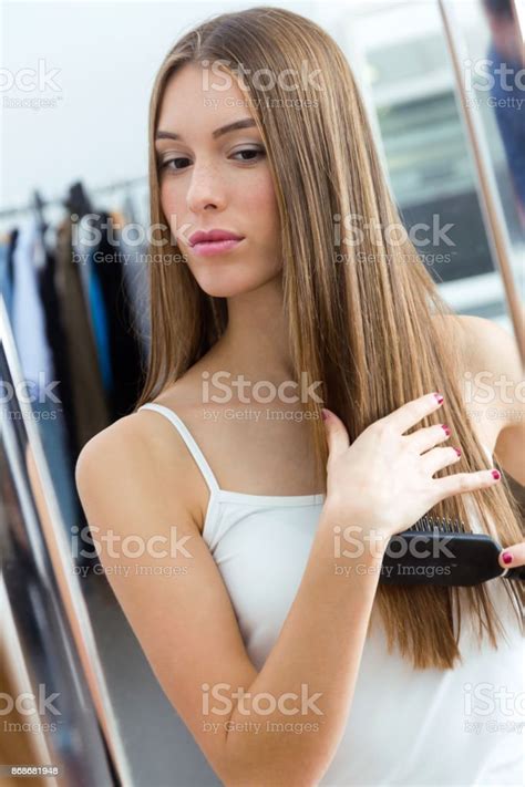 Beautiful Young Woman Brushing Her Long Hair In Front Of Her Mirror