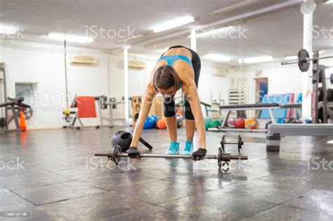 Woman Bending Over In Gym To The Floor And Picking Up Barbell Stock