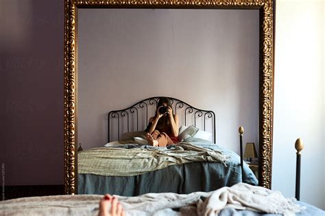 Woman Sitting On Bed Taking Selfie In Mirror By Stocksy Contributor