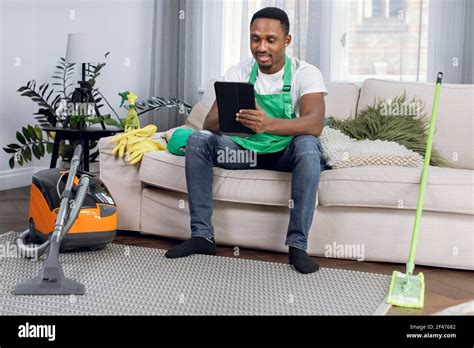 African Cleaner Using Digital Tablet While Relaxing On Couch Stock