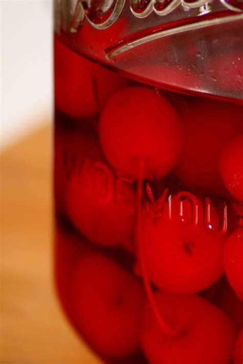 A Jar Filled With Red Cherries Sitting On Top Of A Wooden Table