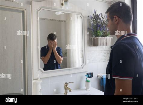 Young Man Standing In Front Of The Mirror Sees Himself In Desperate Reflection With His Hands In