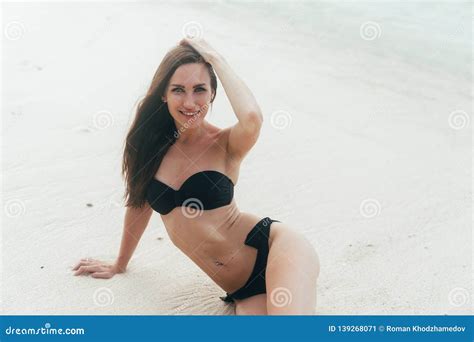 Tanned Girl In Black Swimsuit Posing On Sandy Beach Near Ocean