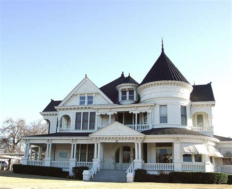 A Large White Victorian Style House With Black Roof