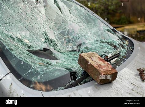 brick sits on smashed windshield of a car with broken glass everywhere the car has been broken
