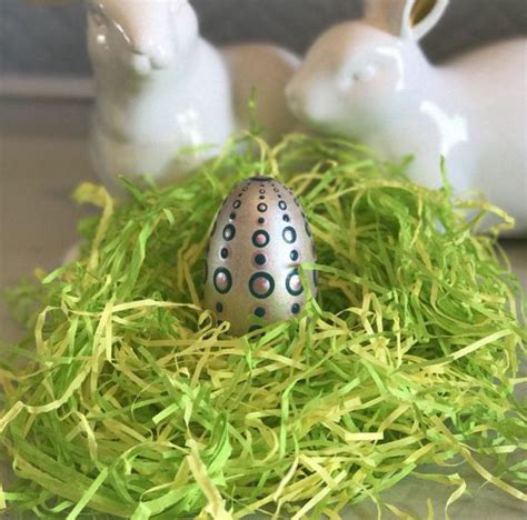 Two White Bunny Figurines Sitting Next To An Egg In Some Green Shredded