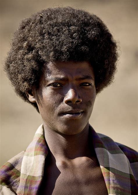 A Man With An Afro Standing In Front Of A Dirt Field And Looking At The
