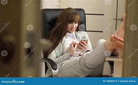 beautiful businesswoman with phone sits in a chair with bare feet on the table resting girl at