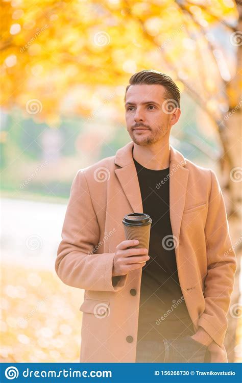 Young Man Drinking Coffee With Phone In Autumn Park Outdoors Stock