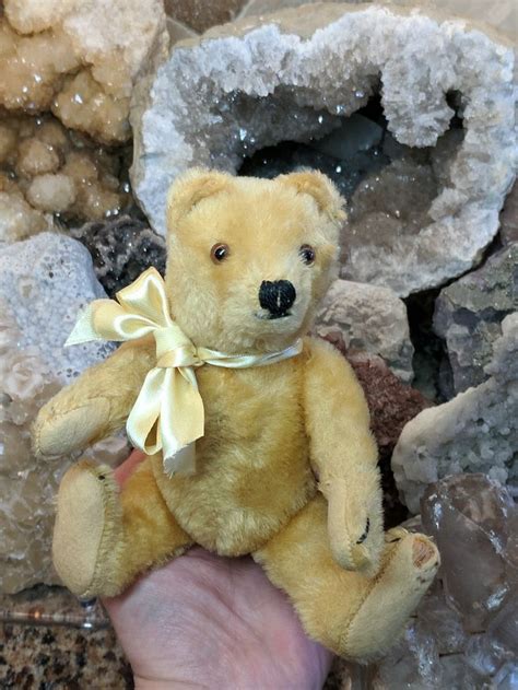 A Hand Holding A Small Yellow Teddy Bear In Front Of Some Rocks And